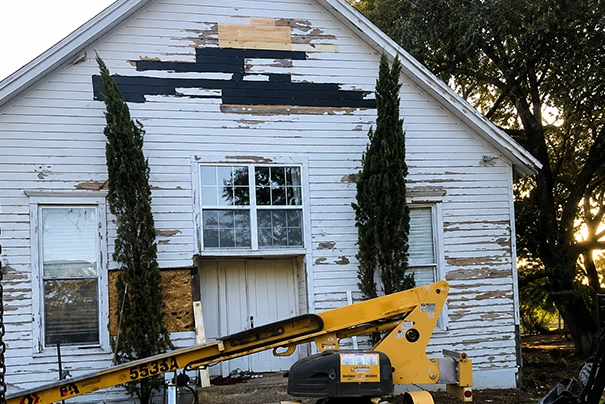 Old Wooden House with Chipping Paint and Construction Equipment in Front