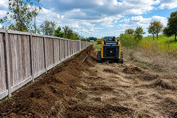 Excavator Performing Drainage Improvements in Waco TX Beside Wooden Fence